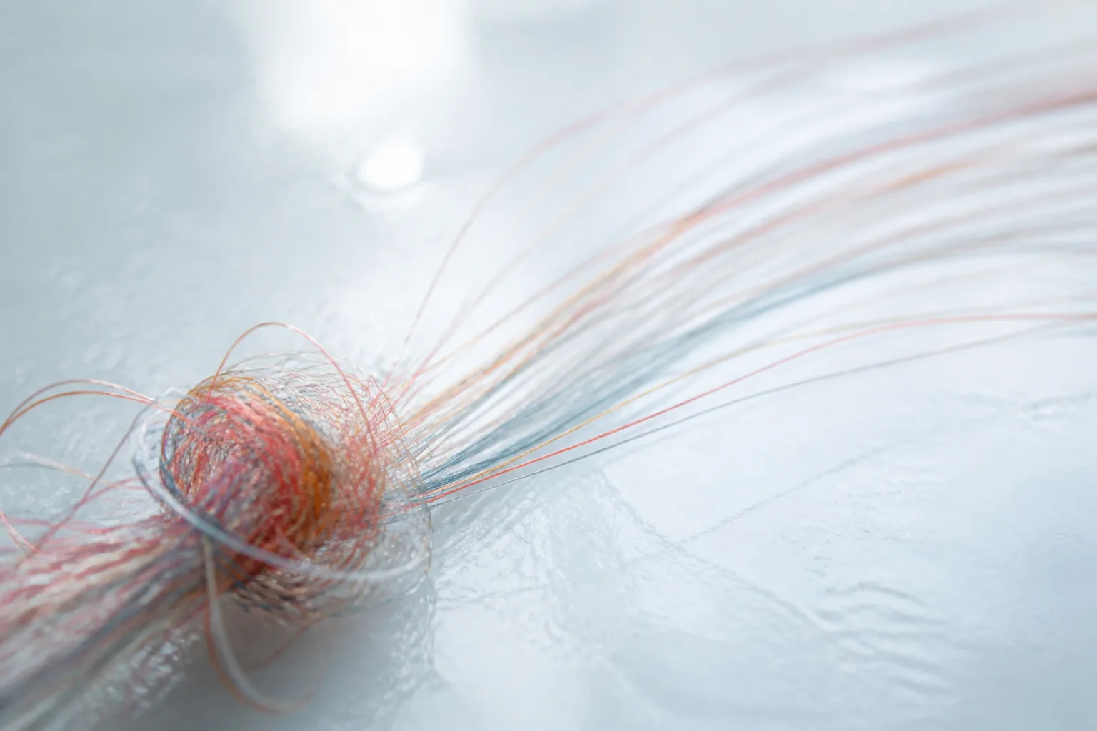 Nudo de hilos translúcidos que se transforma en líneas fluidas sobre una superficie clara