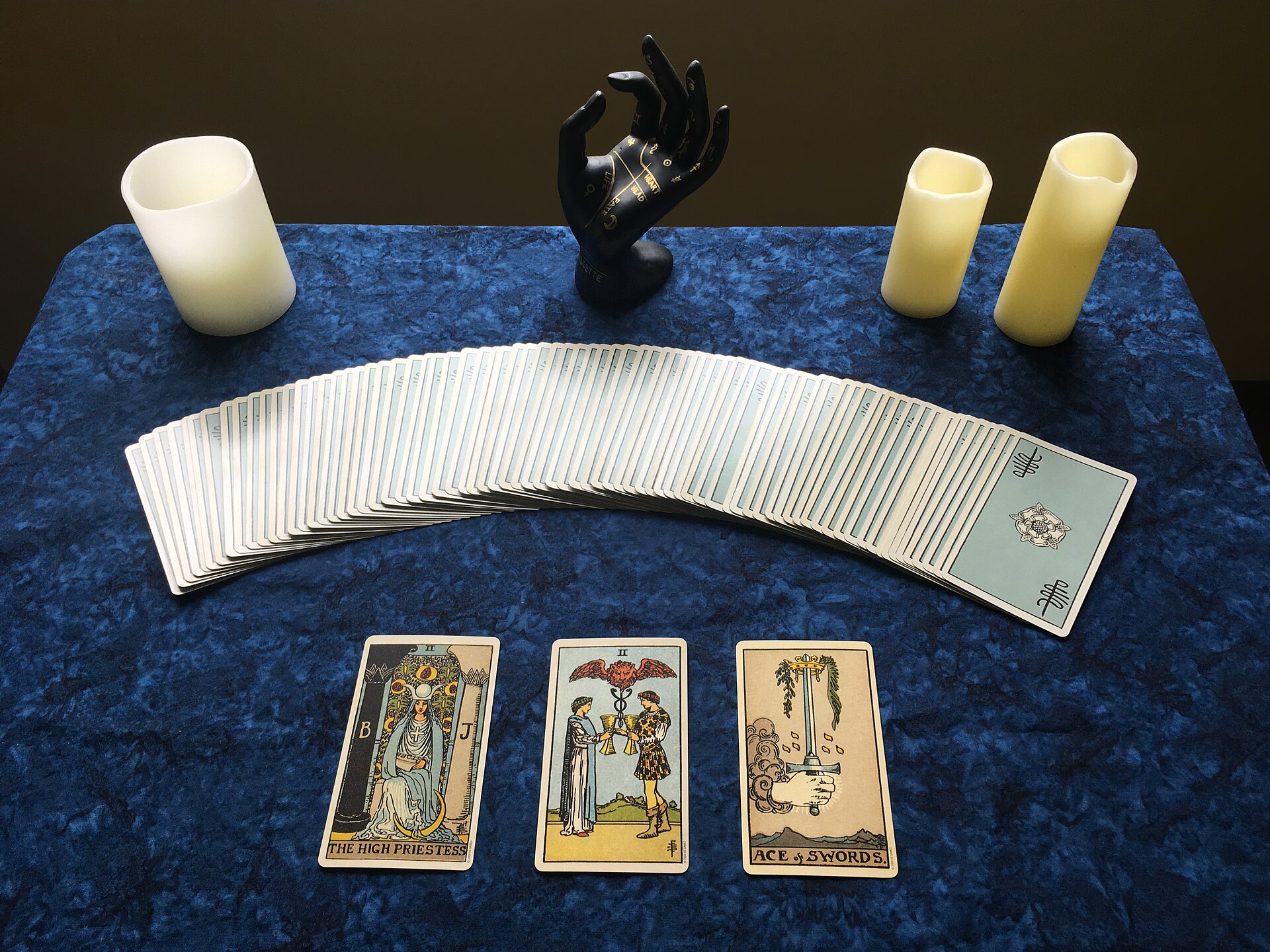 Tirada de tres cartas de tarot con la baraja en abanico y velas, sobre un paño azul